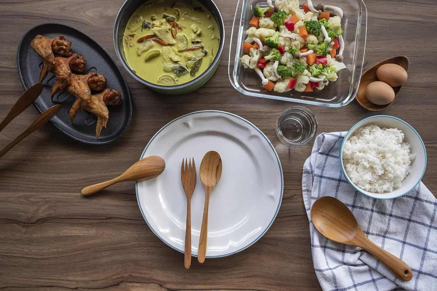 Delicious Asian dinner featuring chicken skewers, rice, vegetables, soup, and eggs on wooden tabletop.