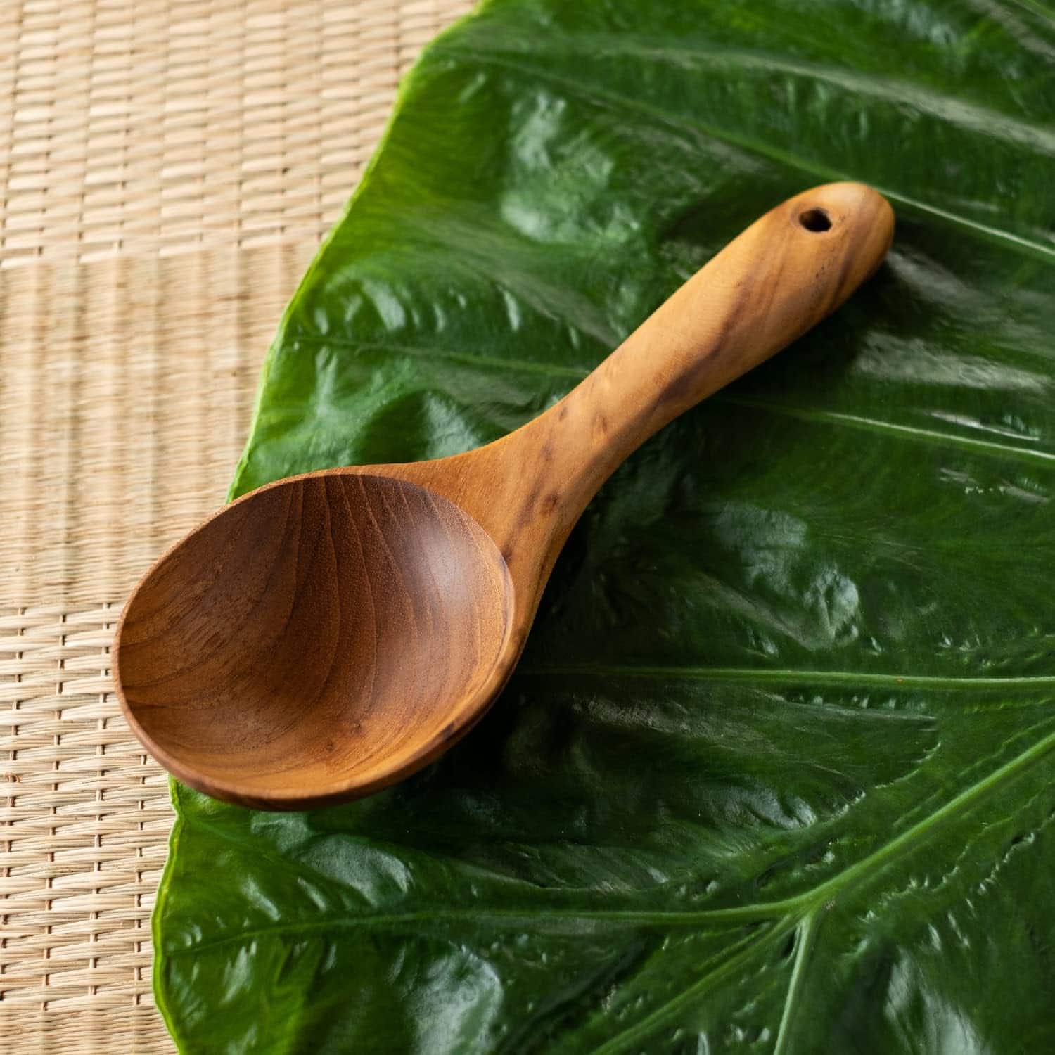 A handcrafted wooden scoop placed on a glossy green leaf, ideal for eco-friendly kitchenware.