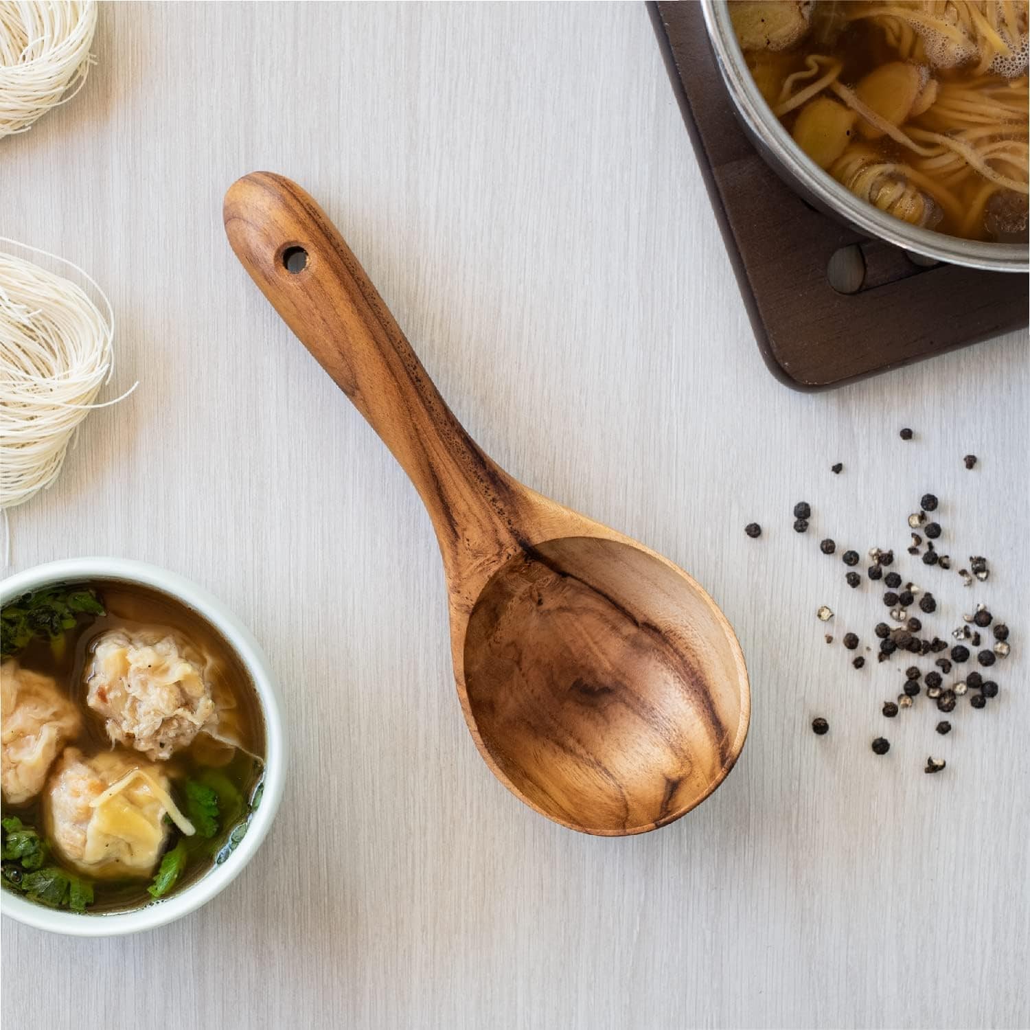 Freshly prepared Asian noodle soup with dumplings, herbs, and black pepper on a white surface.