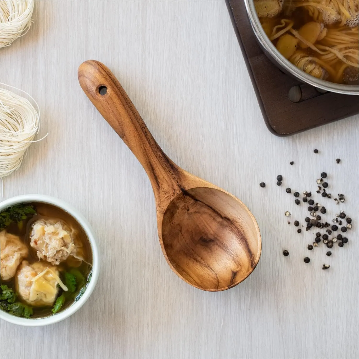 Freshly prepared Asian noodle soup with dumplings, herbs, and black pepper on a white surface.